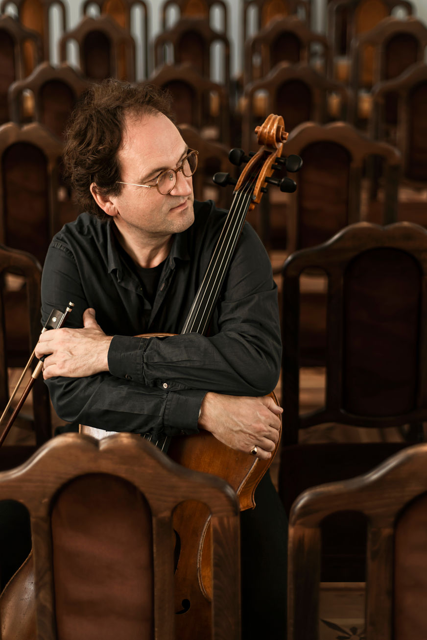 Cellist sitzt im Publikum zwischen vielen braunen Stühlen